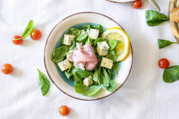 Fresh delicious salad with prosciutto, baby spinach, blue cheese and cherry tomatoes in vintage salad bowl, closeup. Italian style cuisine..