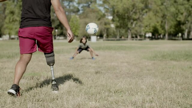 Father with artificial hand playing football with son on lawn. Back view of mans prosthetic leg kicking ball on sunny summer day. Outdoor activity, sport, disability concept