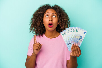 Young african american woman holding euro banknotes isolated on blue background pointing upside with opened mouth.