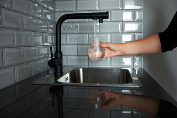 A woman pours tap water into a transparent glass glass. The problem of the purity of tap water. Drinkable tap water.