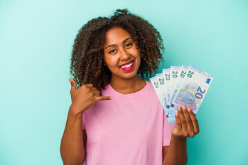 Young african american woman holding euro banknotes isolated on blue background showing a mobile phone call gesture with fingers.