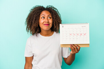 Young african american woman holding a calendar isolated on blue background dreaming of achieving...