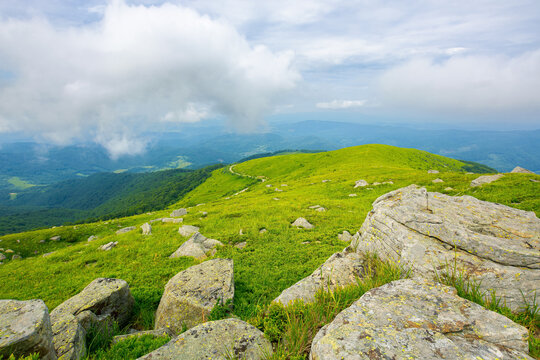 view from runa mountain. huge stones on the grassy slopes. summer landscape of carpathian mountains. bieszczady and vihorlat ridge in the distance beneath a sky low clouds