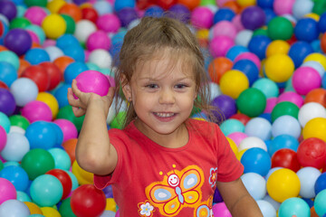 Fototapeta na wymiar Caucasian little girl of five years old looking aside among multicolor balls throwing ball in play center
