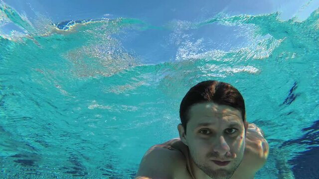 A man swims in a pool underwater. A young white male swims underwater