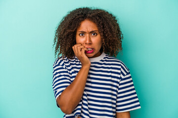 Fototapeta na wymiar Young african american woman with curly hair isolated on blue background biting fingernails, nervous and very anxious.