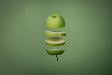 Sliced green apple over green background. Levitating cut apple in the air