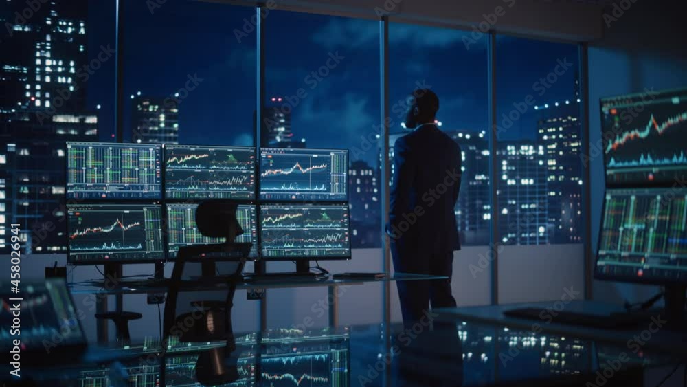 Poster successful businessman looking out of the window on late evening. modern hedge fund office with comp