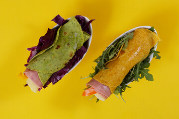 Flour tortilla wraps with ham, cheese and arugula on a yellow background.