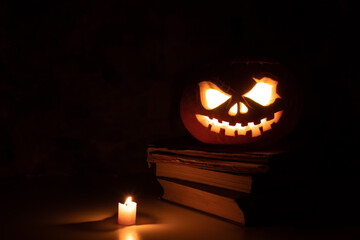 Festive scary halloween pumpkin on a stack of old books with candle