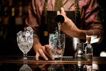 transparent glasses in one of which the hand of man bartender pours drink from jigger