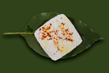 Roasted panela cheese with chile de arbol and olive oil on an avocado leaf with a green, pink, white, purple and yellow background.