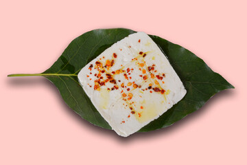 Roasted panela cheese with chile de arbol and olive oil on an avocado leaf with a green, pink, white, purple and yellow background.