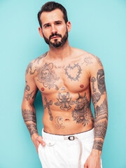 Fototapeta premium Portrait of handsome confident stylish hipster lambersexual model. Sexy modern man. Naked torso with tattoos.Fashion male posing in studio near light blue wall