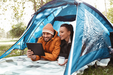 camping, tourism and travel concept - happy couple with tablet pc computer lying inside tent and drinking tea at campsite © Syda Productions