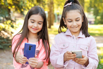 Two happy beautiful sniling kid girls using phone outdoors. Communication consept