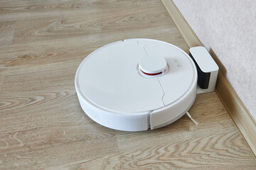 White robot vacuum cleaner at the charging station after cleaning the apartment