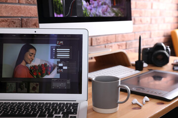 Modern retoucher's workplace with different digital devices on wooden table near red brick wall
