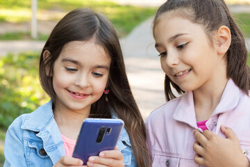 Two happy beautiful kid girls using phone outdoors. Communication consept
