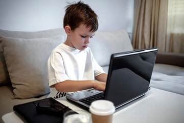 Portrait of teenage Caucasian boy using laptop while studying at home, remote education concept, copy space. Smiling boy looking at laptop. Five years old boy sitting behind a laptop and smiling.