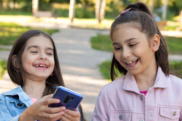 Two happy smiling beautiful kids girls using phone outdoors. Communication consept