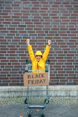 Girl in yellow jacket with arms up in shopping cart with black Friday sign