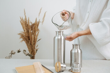 No head image of a woman pouring water in a metal thermos from a jug