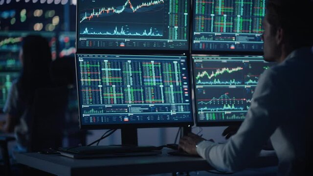 Financial Analysts and Day Traders Working on a Computers with Multi-Monitor Workstations with Real-Time Stocks, Commodities and Exchange Market Charts. Team of Brokers at Work in Agency. Rack Focus.
