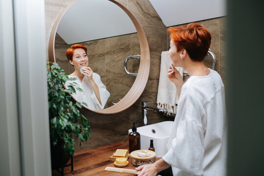 Mirror Image Of A Short-haired Mature Woman Applying Lotion On Her Face