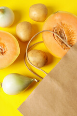 Paper bag with potato, onion and melon on yellow background