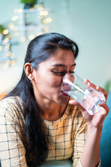 Thirsty young Indian girl drinking glass of pure water during summer - concept of hydration,...