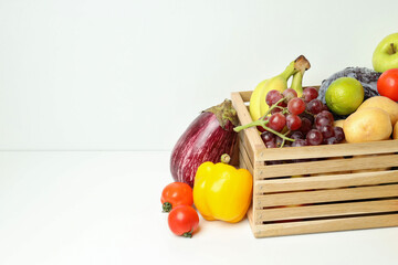Wooden box with different vegetables and fruits on white table