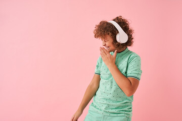 Child boy in stylish clothes wearing headset listening to music and dancing