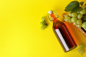 Bottle of vinegar and basket with grape on yellow background