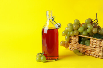 Bottle of vinegar and basket with grape on yellow background