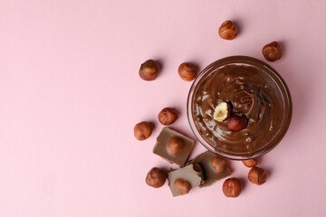 Bowl with chocolate paste, nuts and chocolate on pink background