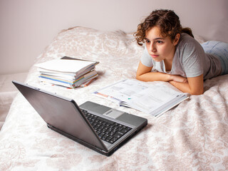 Teenager girl studying online at home. School girl with lap top on the bed. Home education