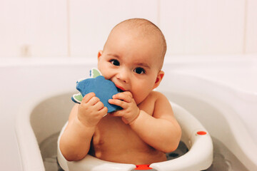 Sweet funny baby taking a bath. Baby chewing a toy in a bath chair. Safety bathing.