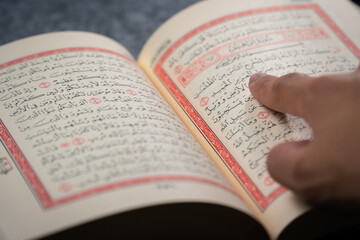 Quran (Koran) - close up of holy book of Muslims, with hand pointing ayat (Āyah).