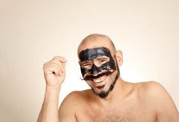 Caucasian man looks at smiling camera with black face mask on his face. Bald adult with mustache Concept health and wellness, skin care.