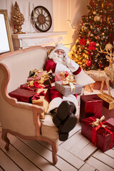 Santa Claus sitting on couch and talking on mobile phone near the fireplace and christmas tree with gifts. New year and Merry Christmas , happy holidays concept