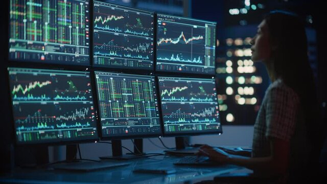 Portrait of a Financial Analyst Working on Computer with Multi-Monitor Workstation with Real-Time Stocks, Commodities and Exchange Market Charts. Businesswoman at Work in Investment Broker Agency.