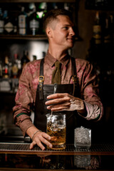 hand of man bartender holds long bar spoon and gently stirring cold drink into mixing cup