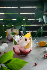 Cold summer tea with ice, currant, lemon and syrup on a green and gray background