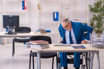 Old male employee in wheel-chair sitting in the office