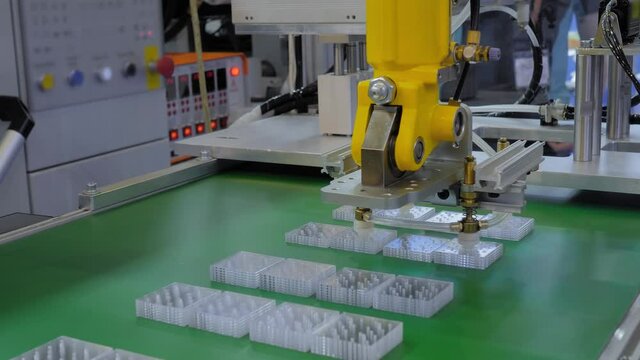 Pick and place yellow robotic arm manipulator moving flat plastic details on conveyor belt at modern robot trade show, exhibition. Manufacturing, industrial, ai, automated technology concept