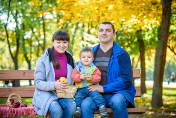 Fototapeta premium happy family enjoying autumn picnic. Father mother and son sit on bench with apples basket. Happy family leisure together concept