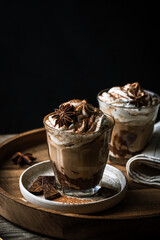 Two glasses of Pumpkin pie spice mocha latte with whipped cream and dark chocolate on plate on wooden tray on dark background .