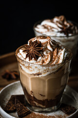 Two glasses of Pumpkin pie spice mocha latte with whipped cream and dark chocolate on plate on wooden tray on dark background .