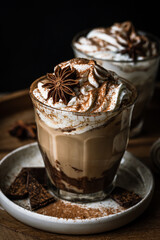Two glasses of Pumpkin pie spice mocha latte with whipped cream and dark chocolate on plate on wooden tray on dark background .